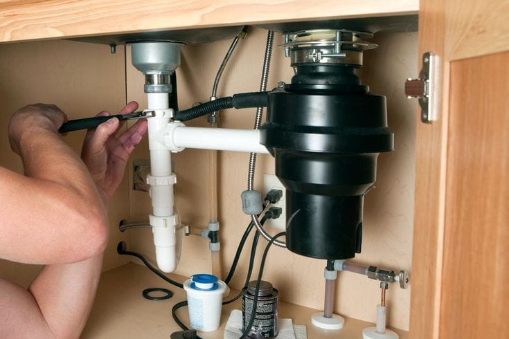 Plumber installing a garbage disposal beneath a kitchen sink in Palm Coast